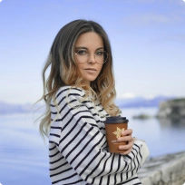 Person holding a cup of coffee by a lake in cool weather