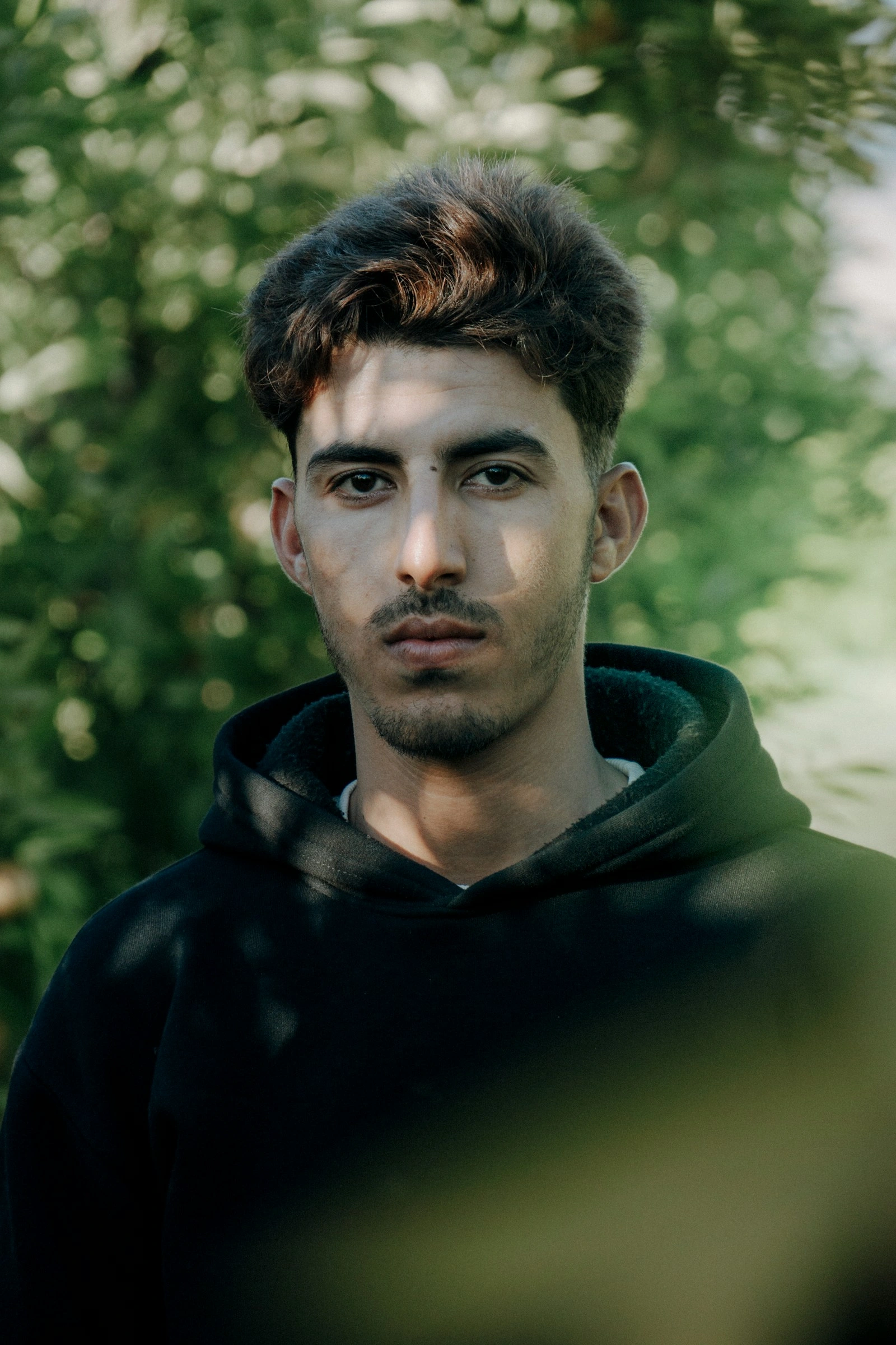 Outdoor portrait of a person in a dark hoodie with a green background