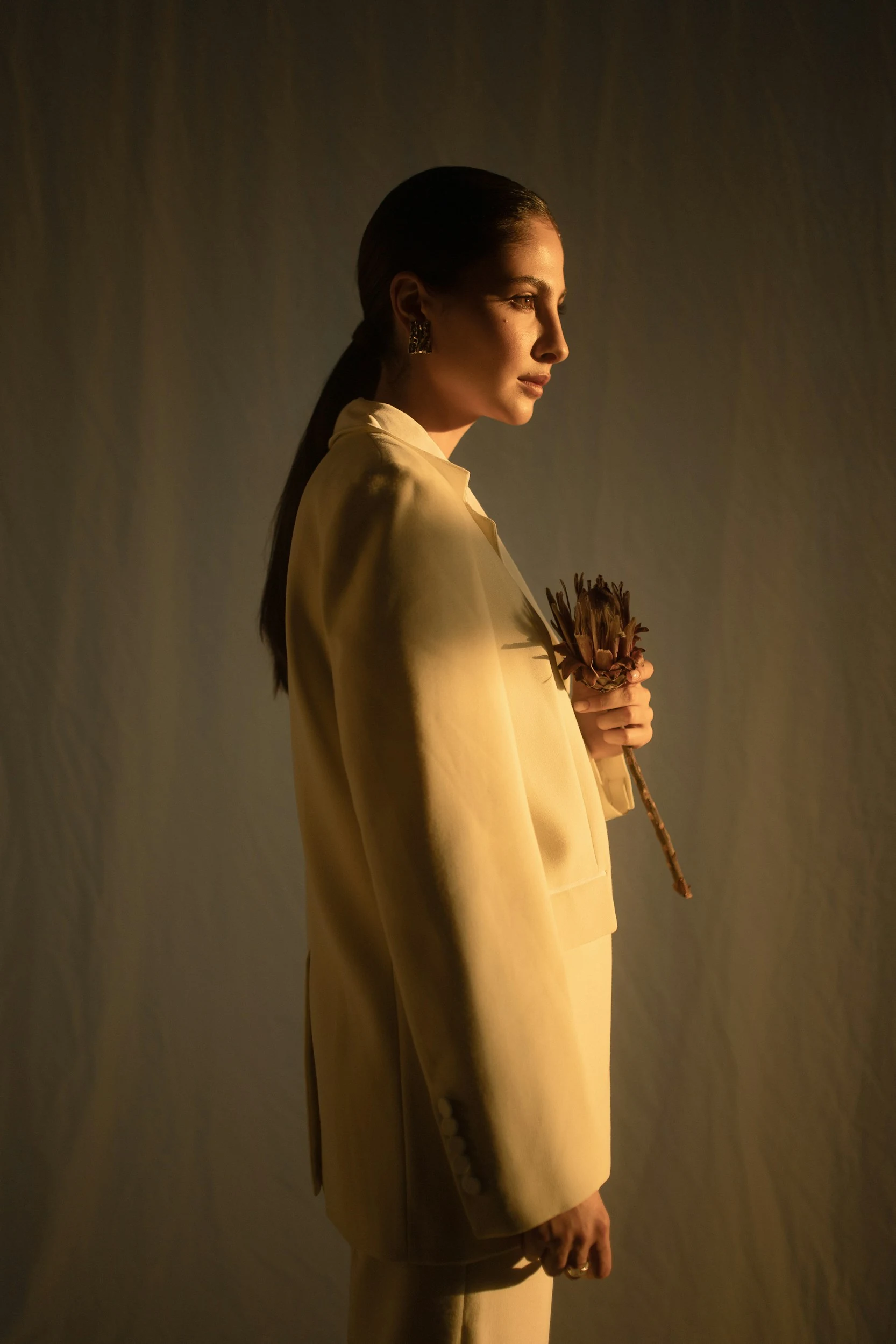 Profile portrait of a person in light clothing holding dried flowers