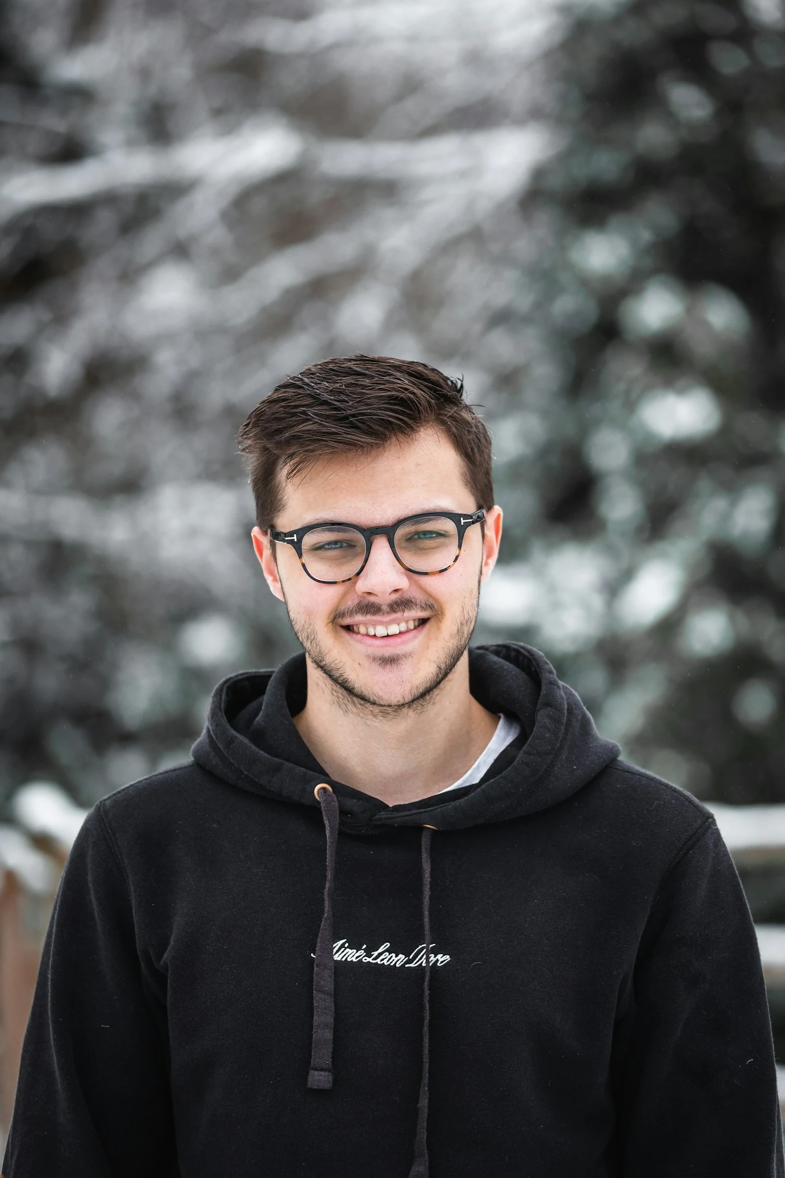 Smiling portrait of a person wearing glasses with snowy trees in the background